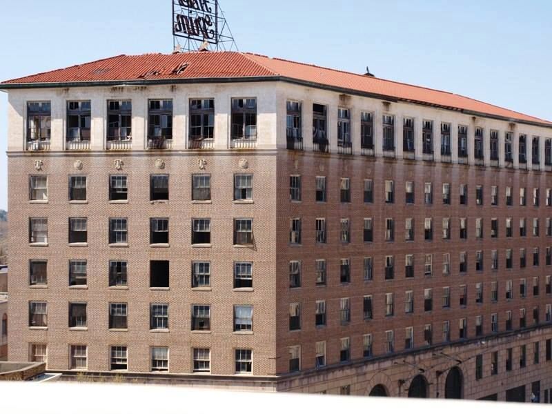 Abandoned multi-story brick building with broken windows, red tile roof, and a sign on top.
