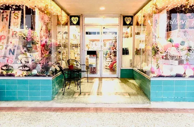 A flower shop with glass windows, a teal base, and a small table and chairs in front.