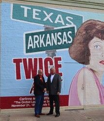 Two men stand in front of a mural: 