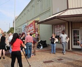 People gather outside a building with a mural. Some are near the entrance.