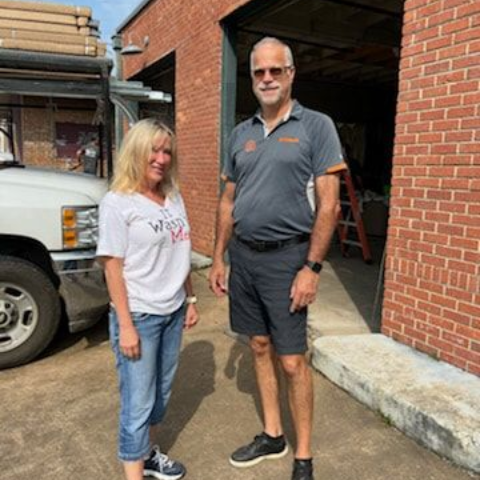 Woman and man stand outside a brick building with a truck.