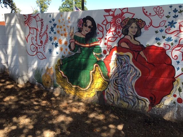 Mural on a wall depicting two women in colorful dresses with floral decorations.
