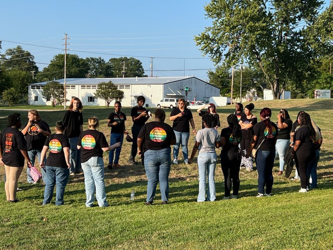 Group of people in black shirts standing outdoors, some with hands on their chests.