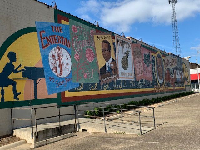 Mural on a building, depicting colorful posters and figures. An outdoor scene with a blue sky.