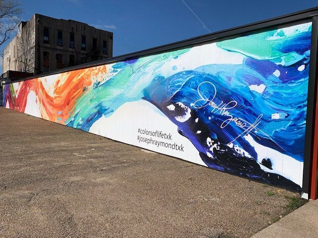 Mural with colorful abstract brushstrokes and signature on a building wall.