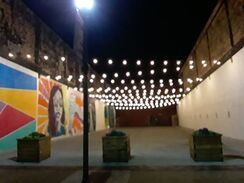 Nighttime outdoor space with string lights, murals on walls, and planters.