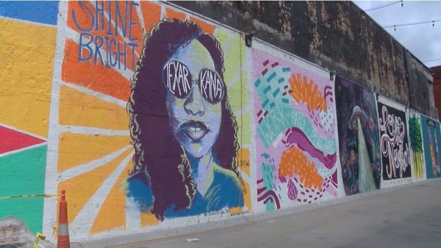 Colorful murals on brick wall, including one with a portrait of a person wearing sunglasses, and the words