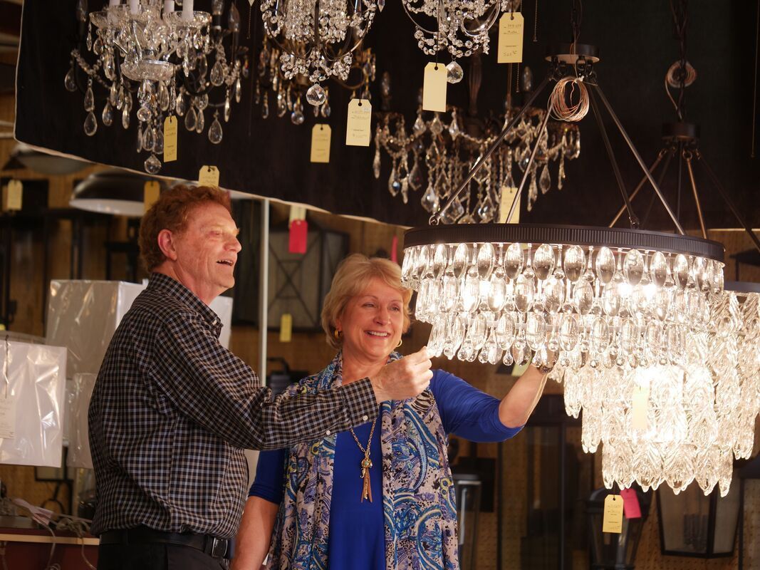 Couple admiring a chandelier in a showroom, smiling. Other chandeliers hang behind them.