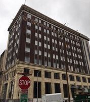 Brown brick high-rise building with a light-colored base, a stop sign is in front.