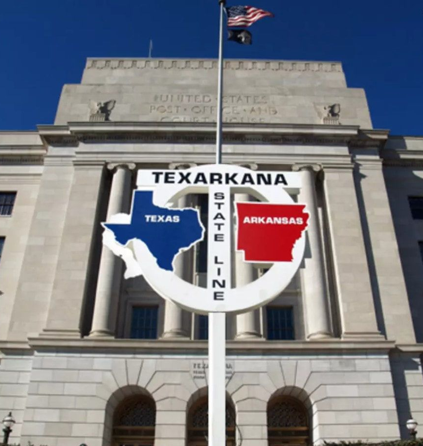 Texarkana state line sign with Texas and Arkansas flags, in front of a US Post Office building.