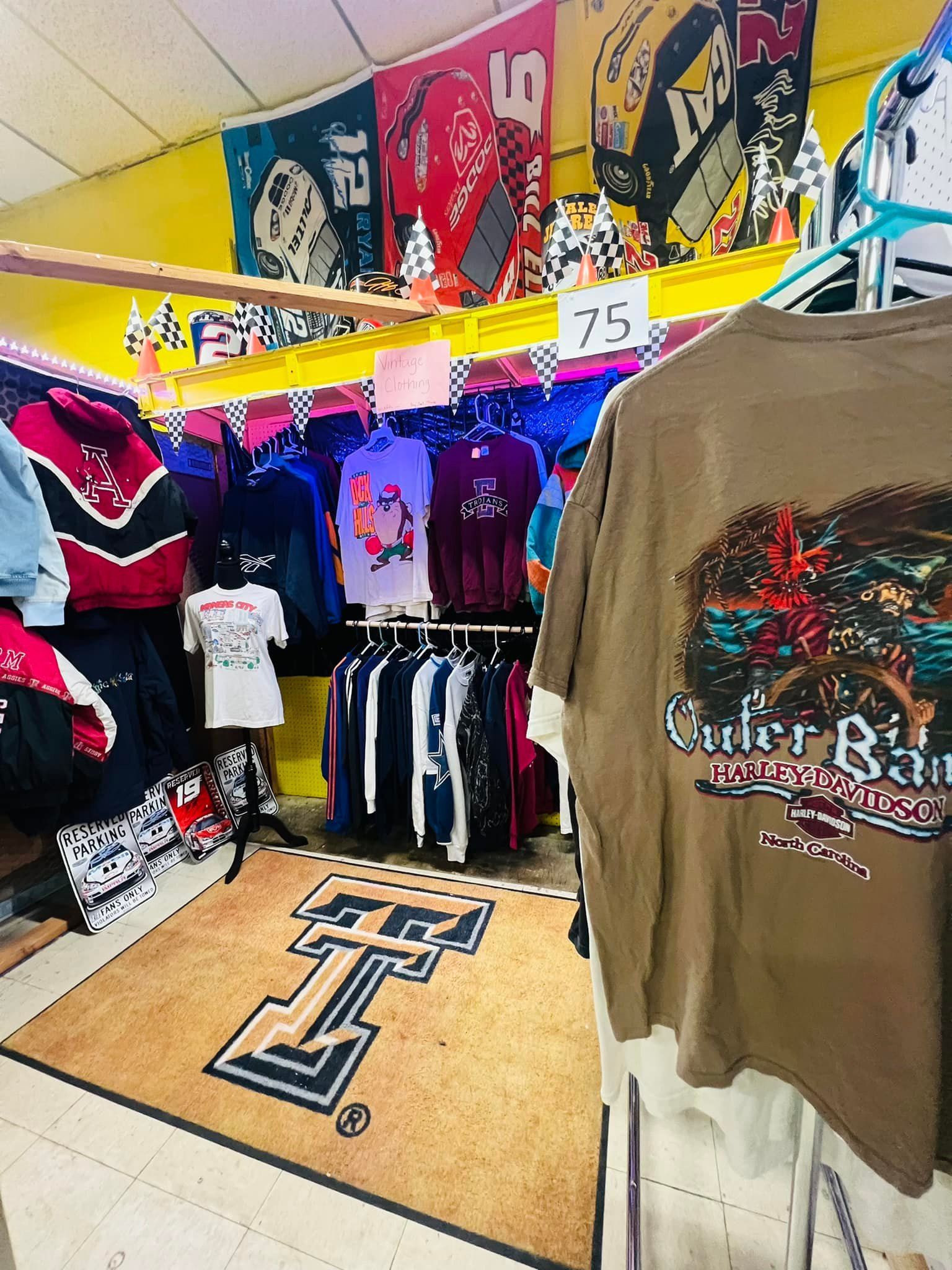 A clothing store with racks of shirts and banners. A Texas Tech rug is on the floor.