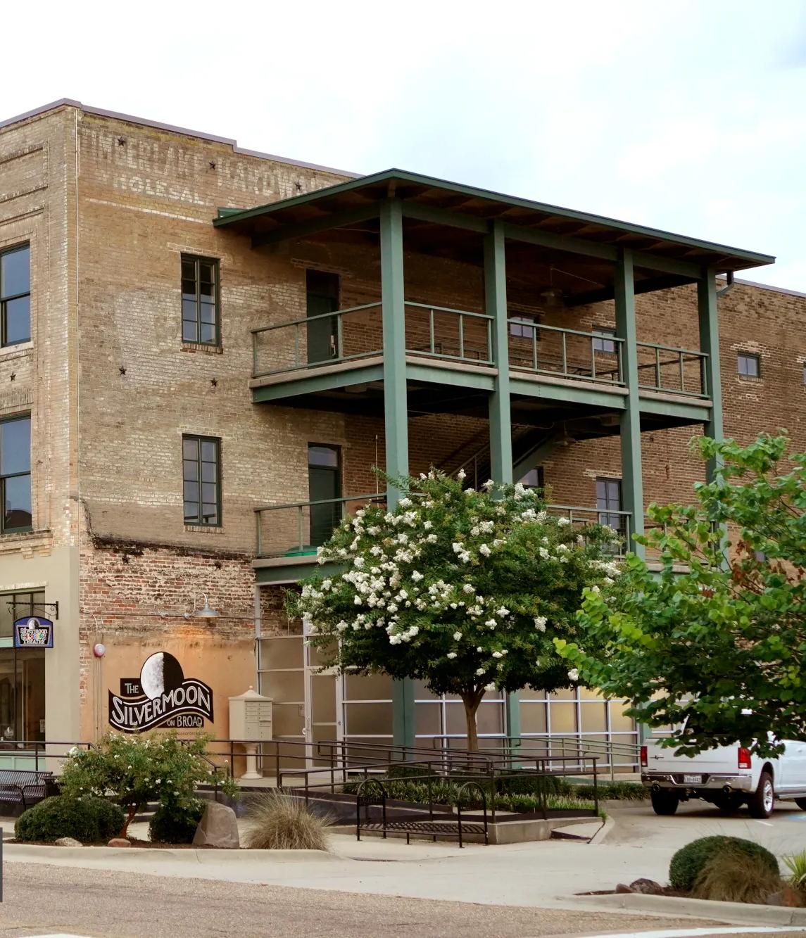 Multi-story brick building with green balcony, storefront, and landscaping.