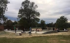 People skateboarding and rollerblading in a concrete skatepark under a cloudy sky.