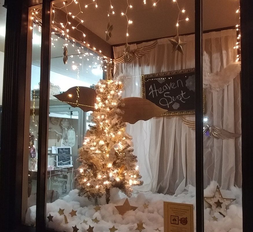 Christmas window display, featuring a lit Christmas tree and angel wings, with string lights and stars.