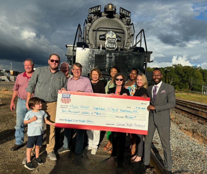 Group holds large check in front of a train, celebrating a donation in Tennessee.