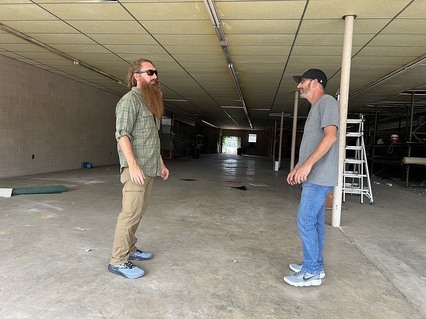 Two men face each other in an abandoned building. One with a beard, the other with a hat.