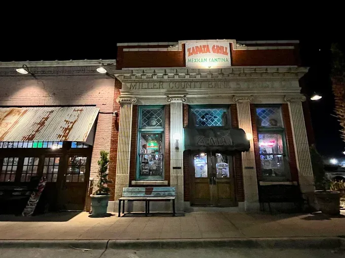 Exterior of Sarita's Grill, a building at night with lit windows, brick facade, and a rustic metal roof.