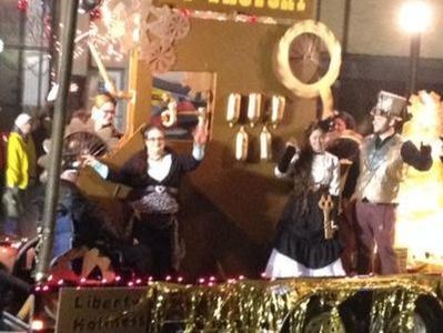 People in steampunk costumes on a holiday parade float decorated with gears and lights.