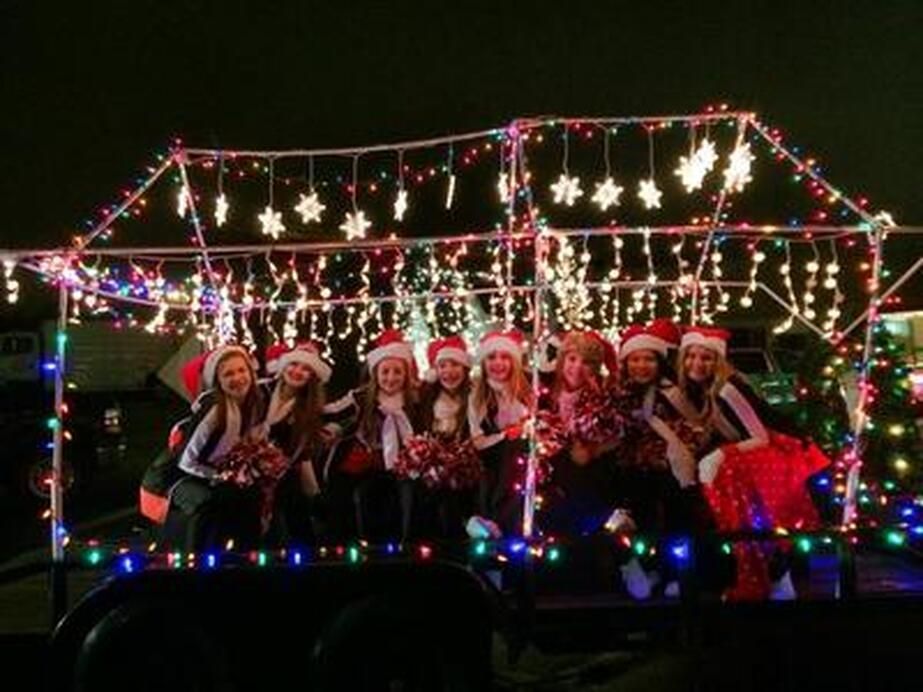 Group of people in Santa hats on a trailer decorated with Christmas lights and stars.