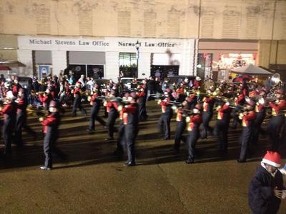 Marching band performs, dressed in red and black uniforms, in front of a law office building at night.