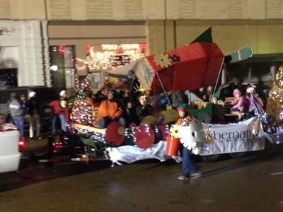 A parade float decorated with a red structure and people, with a person in a white costume carrying something.
