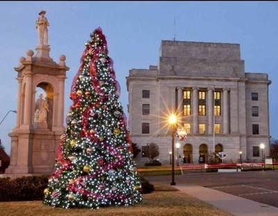 Christmas tree with lights and decorations in front of a courthouse at dusk.
