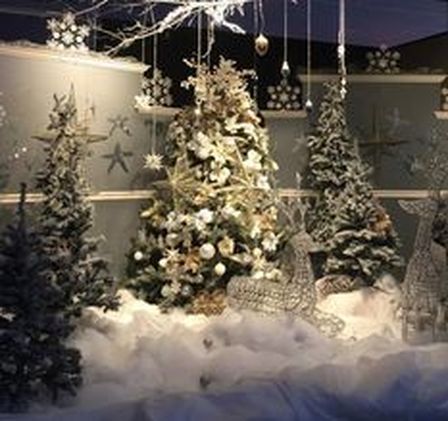 Christmas window display with snowy trees, ornaments, and reindeer decorations.