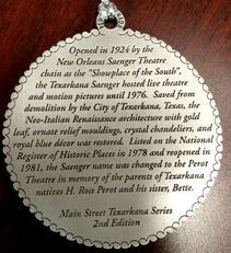 Silver circular plaque with text about the Texarkana Saenger Theatre, including its history and architecture.