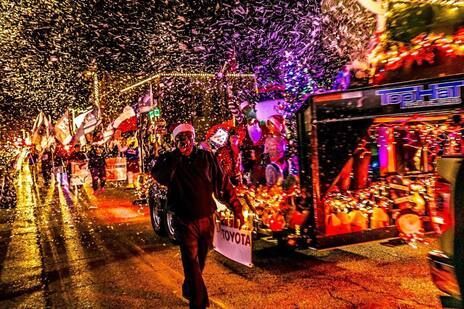 Night parade with illuminated floats, falling confetti, and people walking alongside.