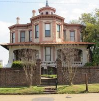Historic house with a brick exterior, a tall, rounded tower, and a low brick wall.