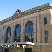 Exterior of a brick and stone building with large arched windows, a small balcony, and blue sky.