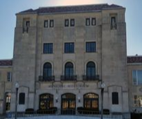 Exterior of the Municipal Auditorium, a light-colored building with dark windows and a tiled roof, under a clear sky.