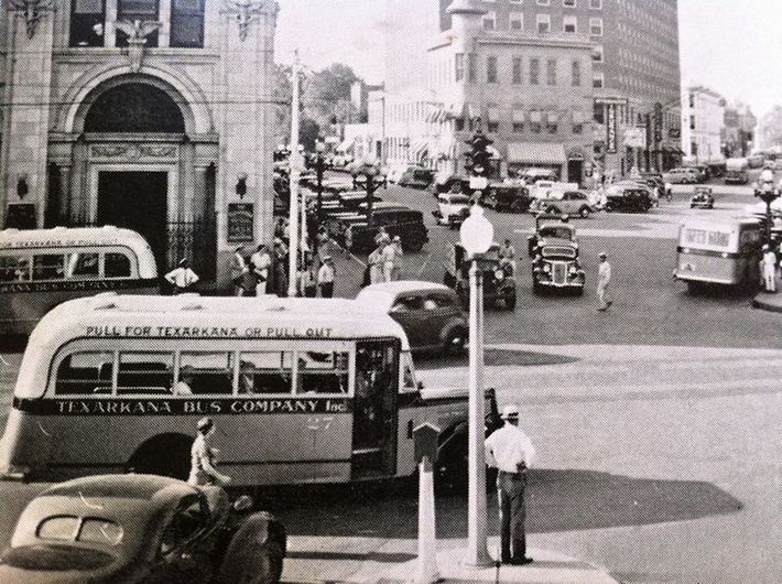 Busy street scene in Texarkana, Texas. Buses, cars, buildings, and a traffic officer.