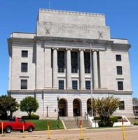 White stone courthouse with columns, under a blue sky. A red car sits in front.