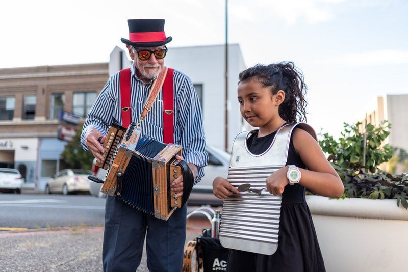 Man playing a concertina with a young person beside him holding a tambourine on a city street.