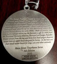 A silver, circular ornament with engraved text about a Texarkana fountain, 2010.