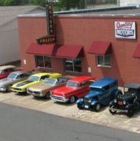 Classic cars parked in front of a Quality Motors dealership.