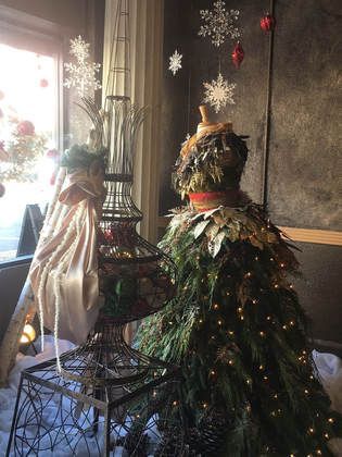 Christmas display: dress form covered in pine needles and lights, next to decorative bird cage.