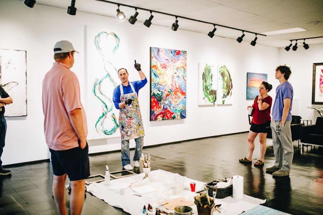 Artist gestures toward artwork, explaining it to a small group in a gallery.