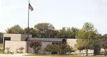 A low, rectangular building with a curved glass roof and American flag in front.