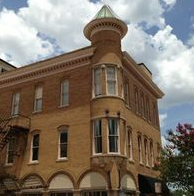 Brick building with a corner turret, arched windows on the bottom floor, and a cloudy sky.