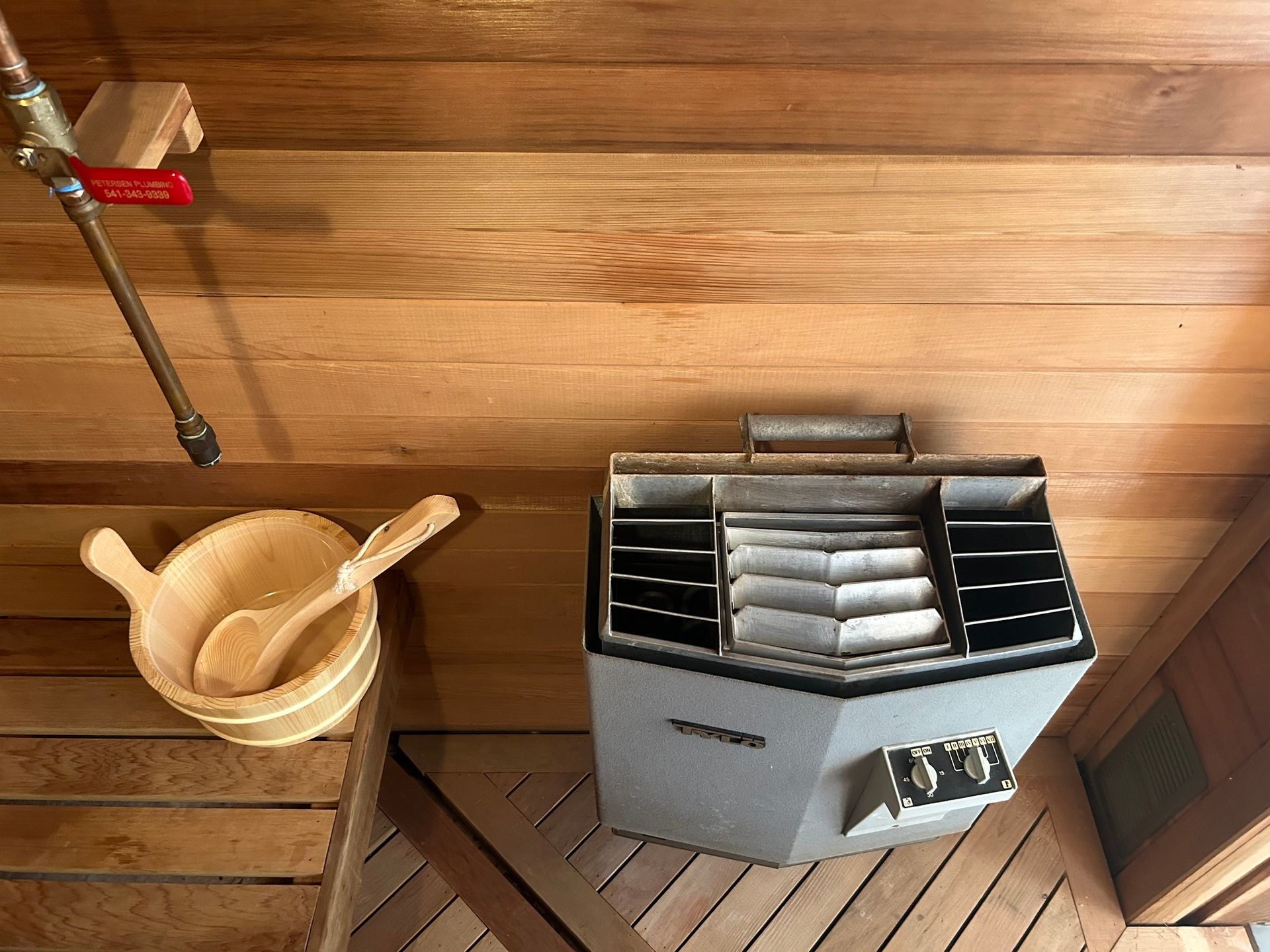 A wooden sauna with a bucket and spoon on the floor.