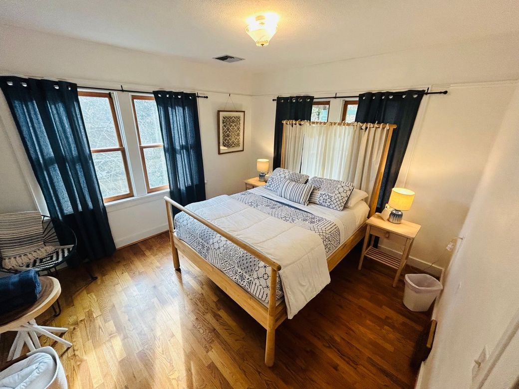 A bedroom with a bed , chair , nightstand , and window.