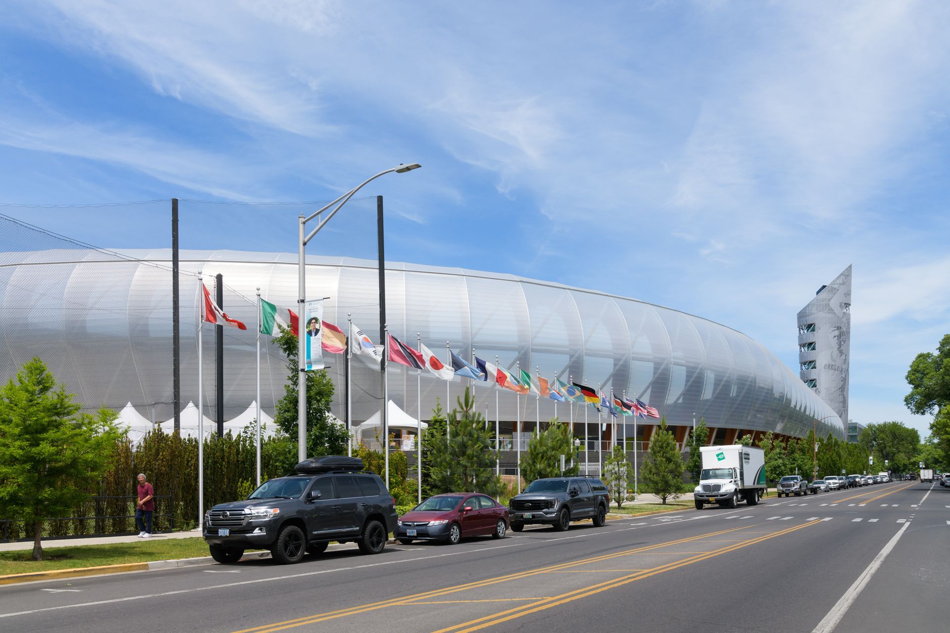 A row of cars are parked on the side of the road in front of a large building.
