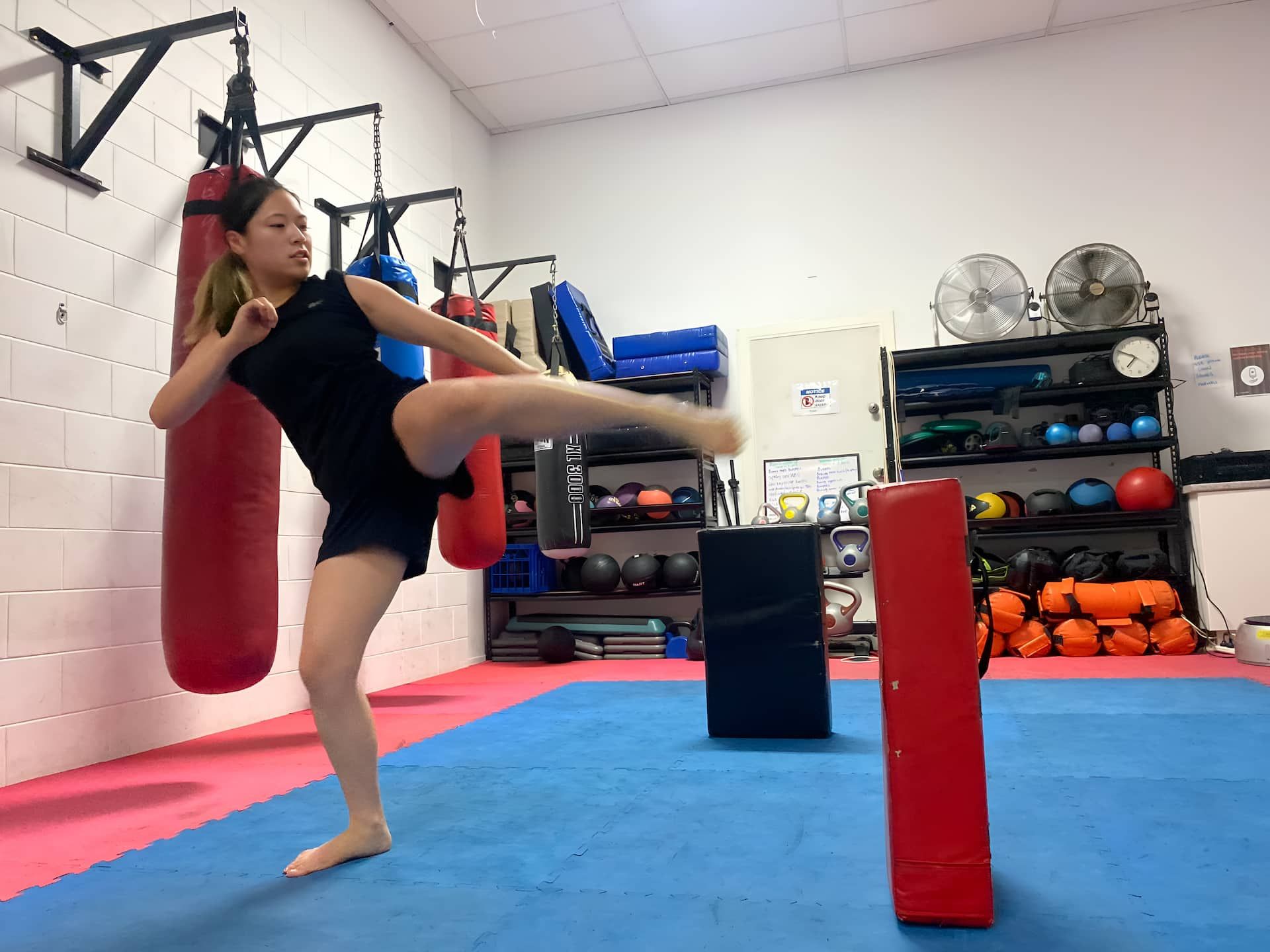 A Girl Trying To Kick The Boxing Bag — Maxenergy Fitness In Smithfield, QLD