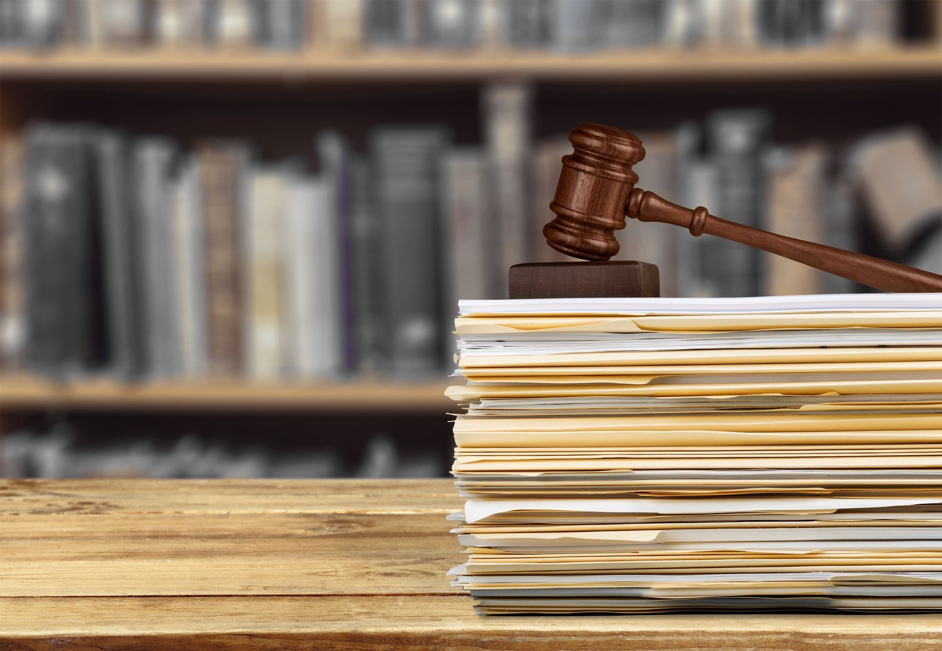 Wooden gavel on stack of documents; bookshelf background.