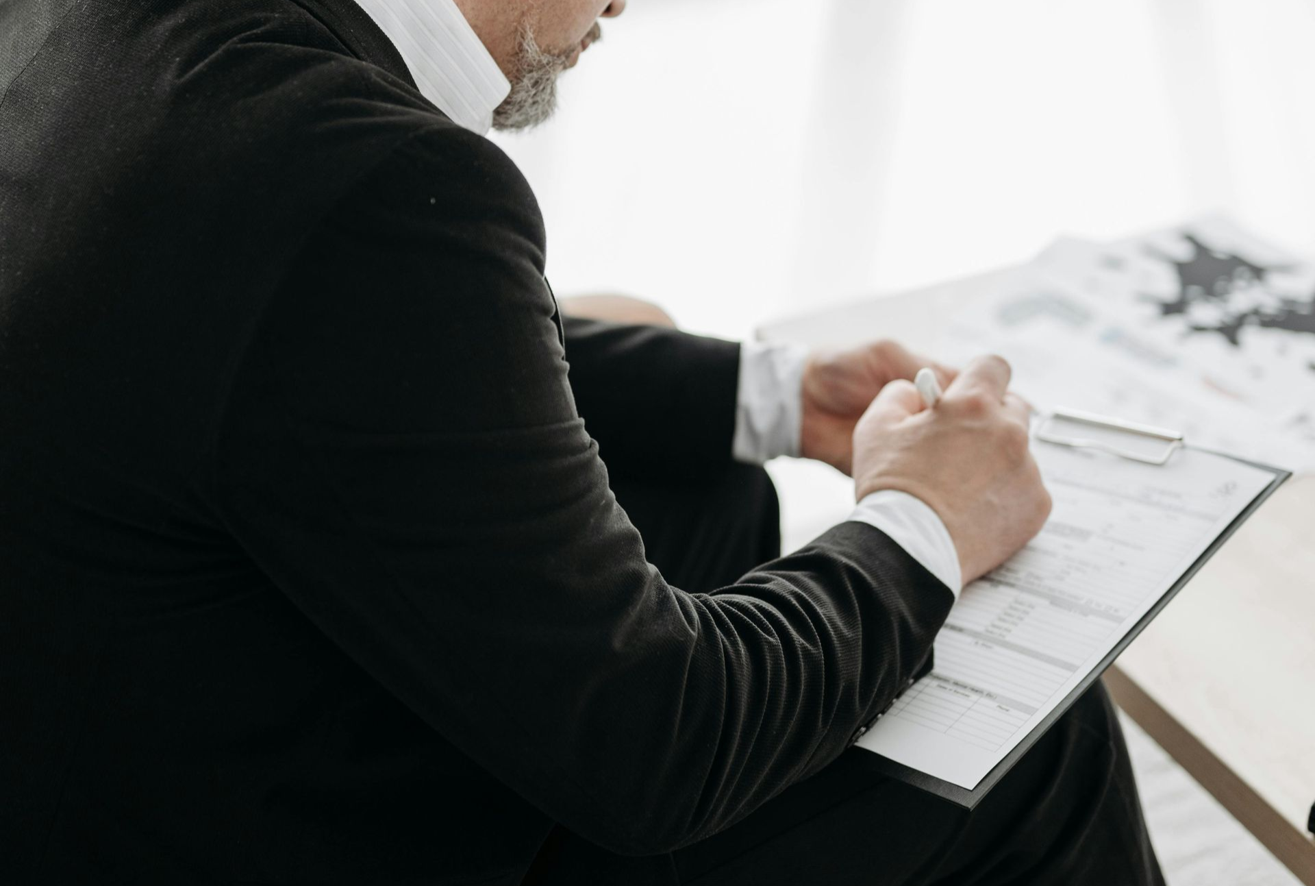 Man in black suit writing on a clipboard.