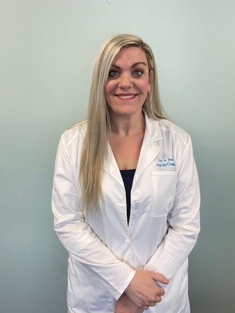 Woman in a white lab coat smiling against a plain gray background.