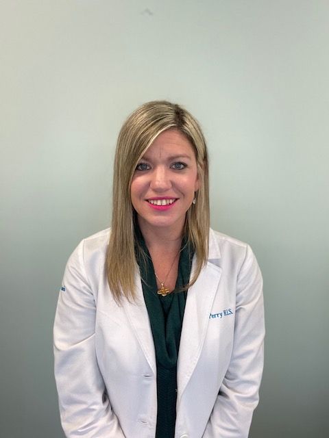 Woman in white lab coat smiling against a plain gray background.