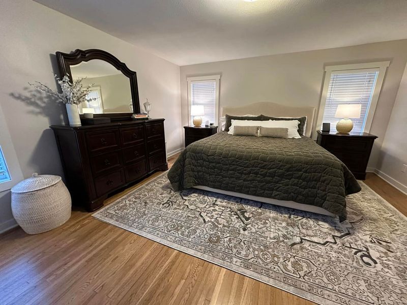 A bedroom with a bed , dresser , mirror and rug.